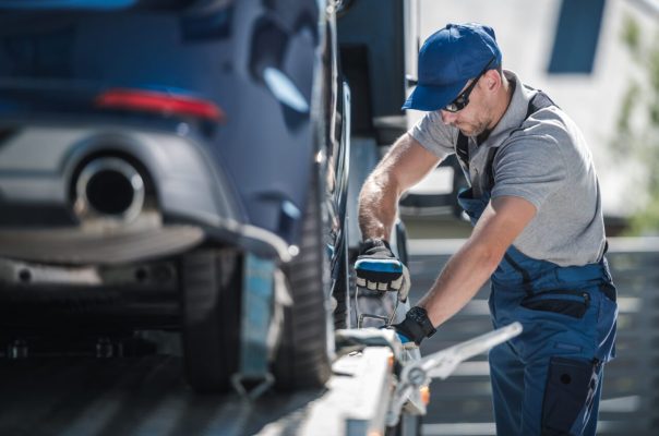 towing-company-worker-securing-vehicle-on-the-truck-platform-e1697119471113.jpg